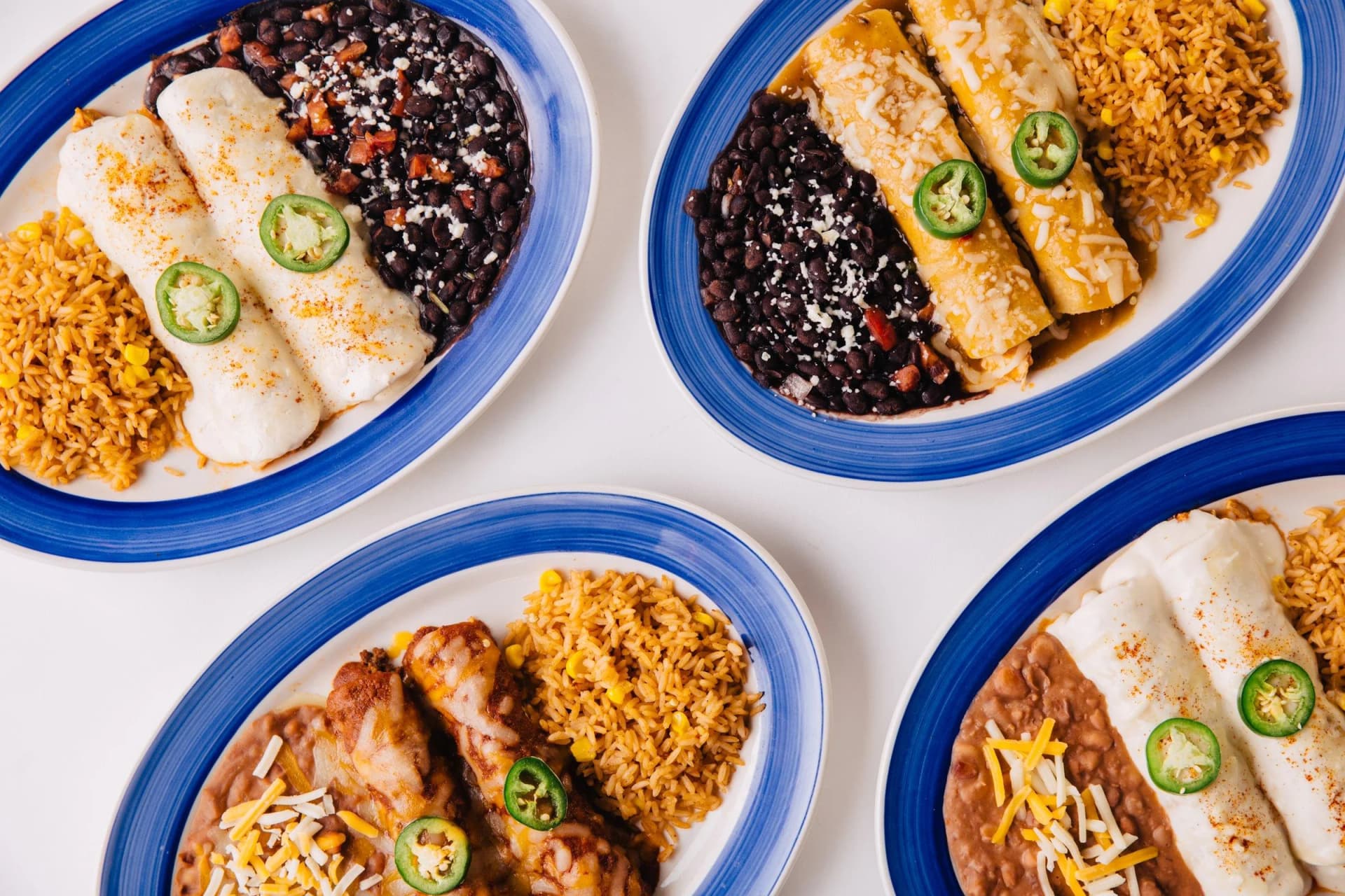 Four plates of enchiladas with rice, beans and sliced jalapeños