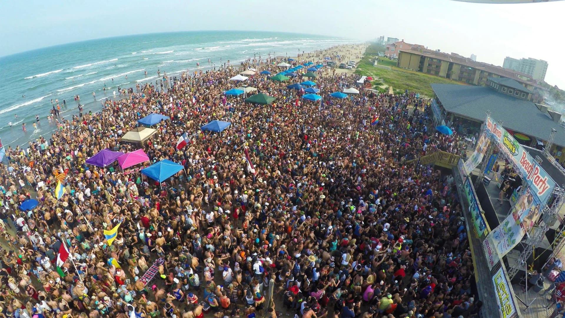 Aerial view of a packed spring break crowd on the beach in front of an outdoor concert stage