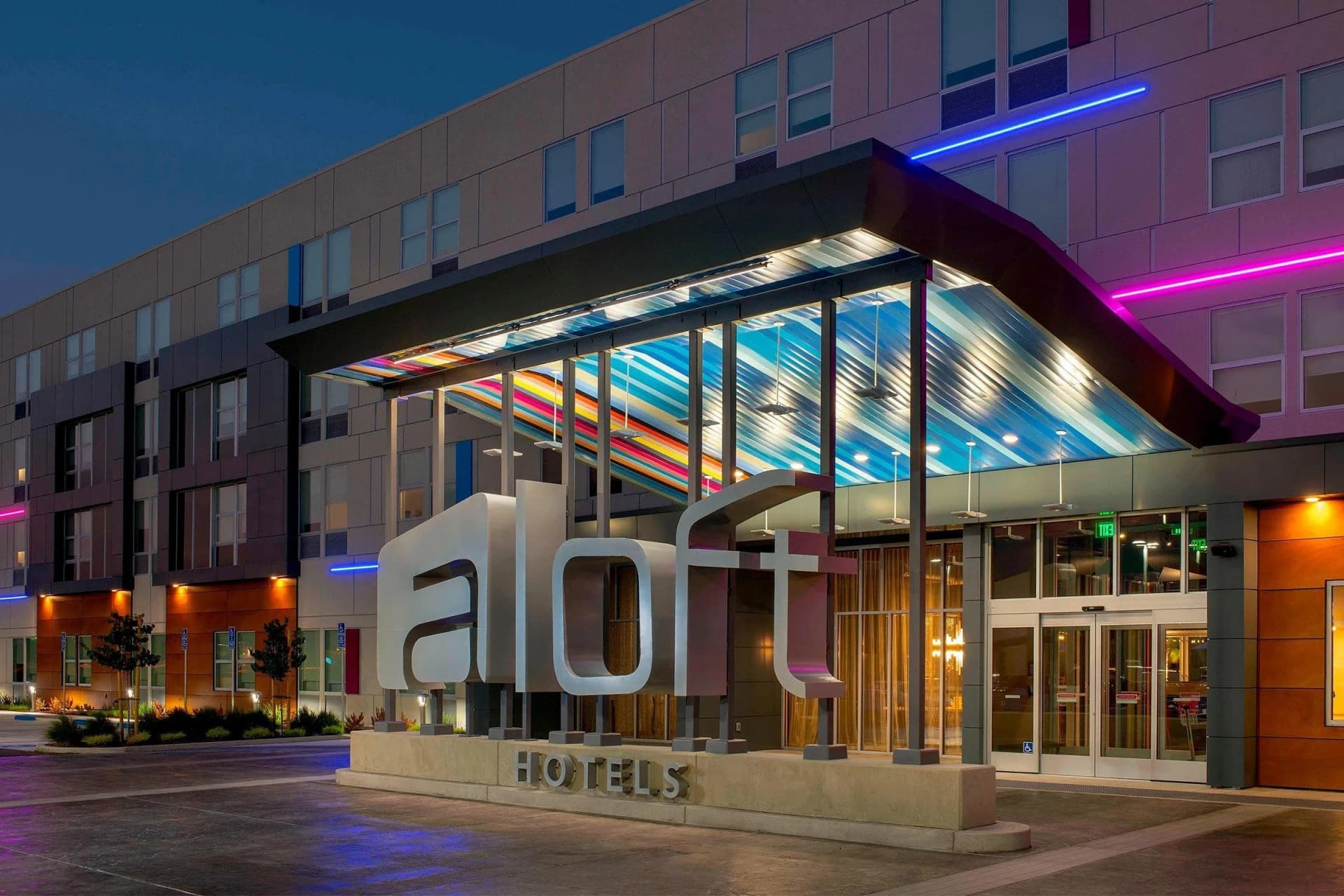 Aloft McAllen entrance at dusk, with the lit Aloft Hotels sign under a striped glass canopy