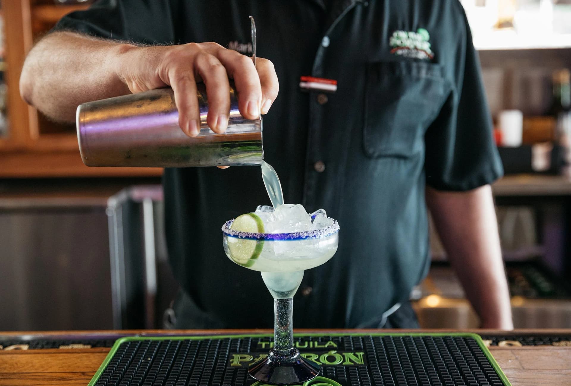 Bartender pouring a frozen margarita into a salt-rimmed glass with a lime wheel
