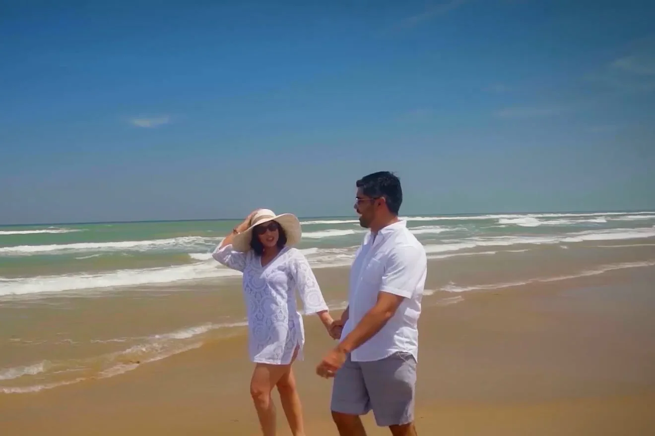 Couple walking hand in hand along the beach at the water's edge on a sunny day