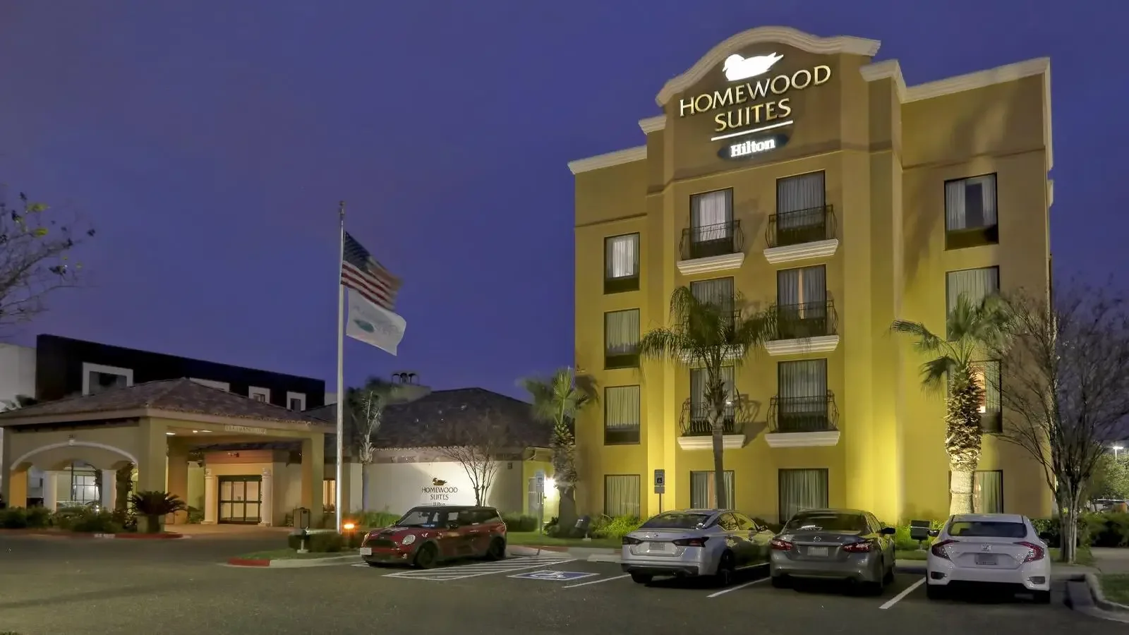 Homewood Suites McAllen lit up at night, with palms and cars parked out front